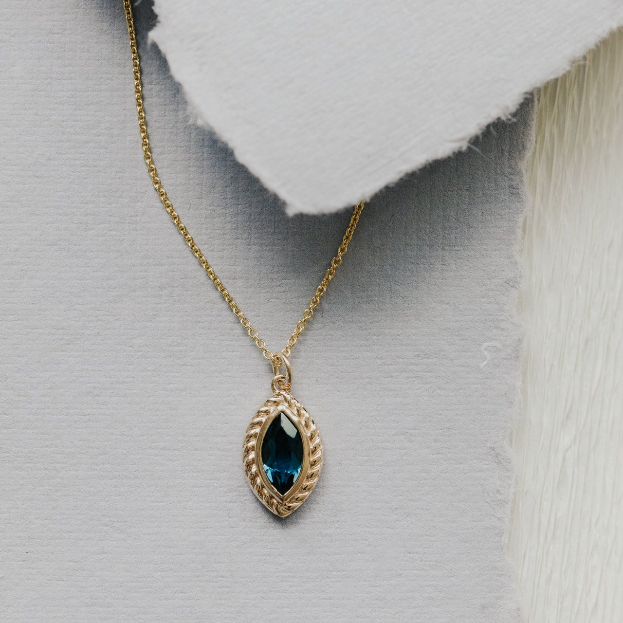 Gold necklace with a London blue topaz pendant on a textured gray background