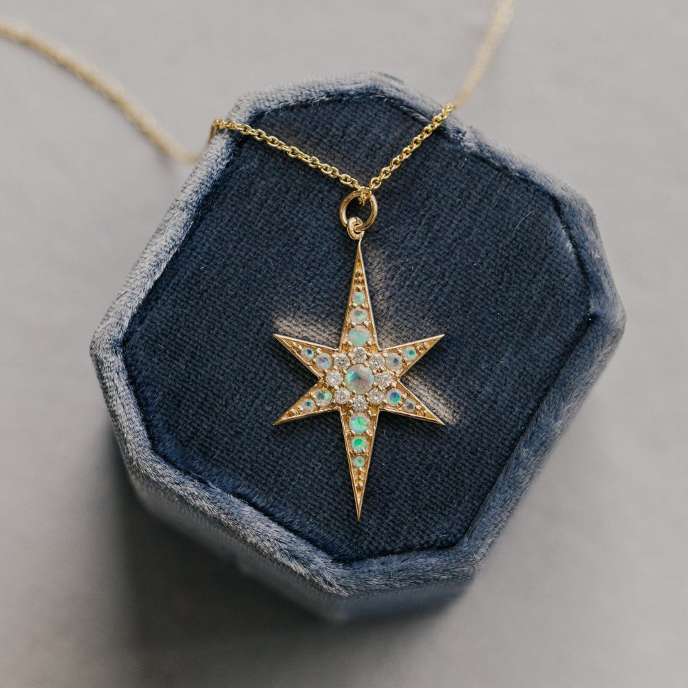 Star-shaped opal and diamond pendant on a gold chain displayed on a hexagonal blue stone