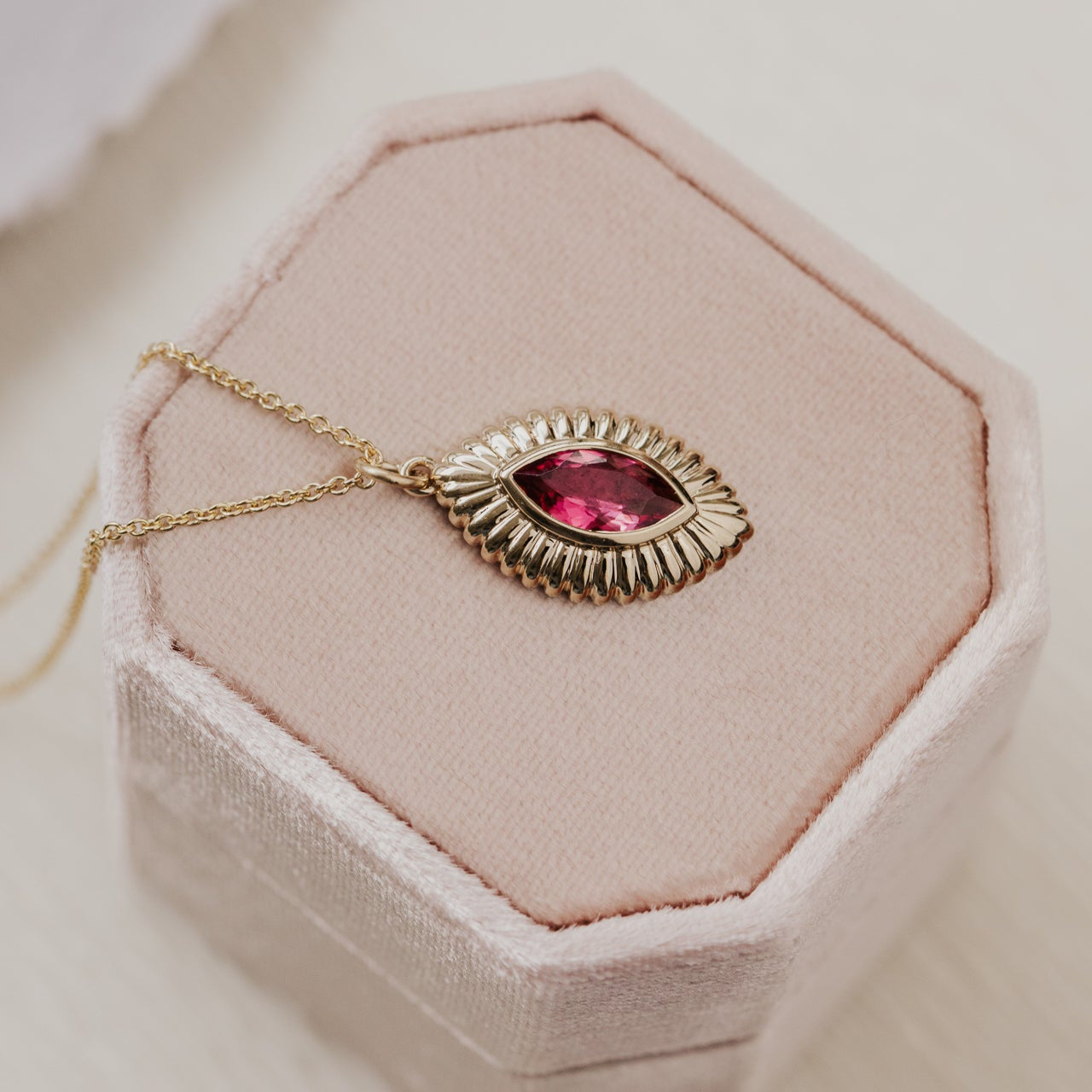 Gold necklace with a pink tourmaline gemstone pendant on a pink cushioned stand.