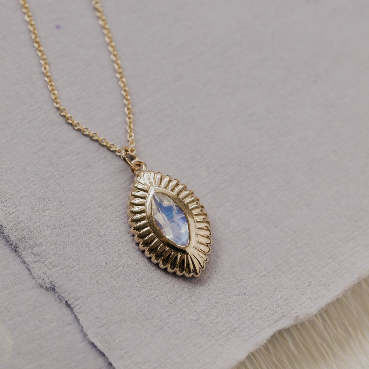 Gold necklace with a moonstone pendant on a textured gray surface