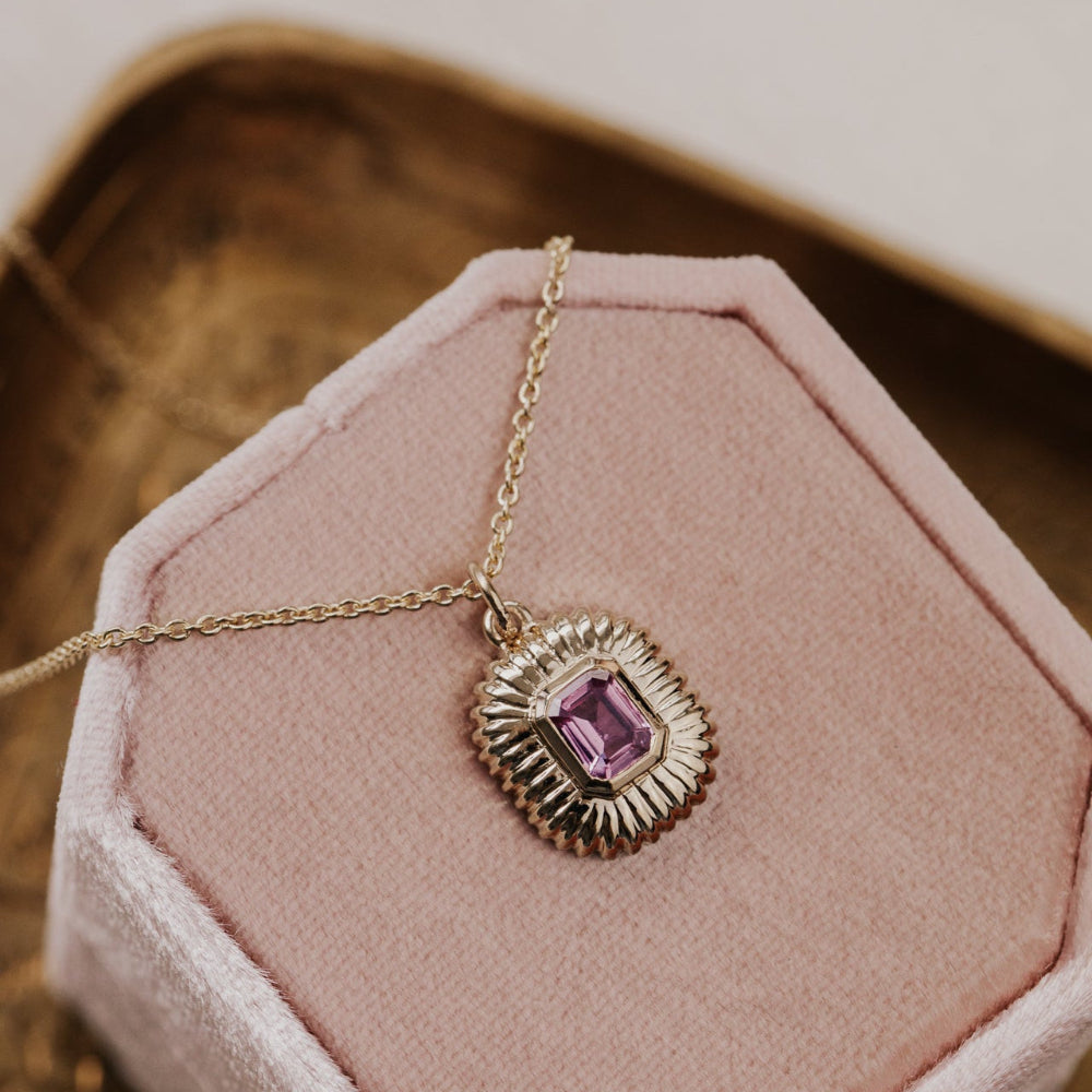 Necklace with a pink sapphire gemstone pendant on a pink cushion
