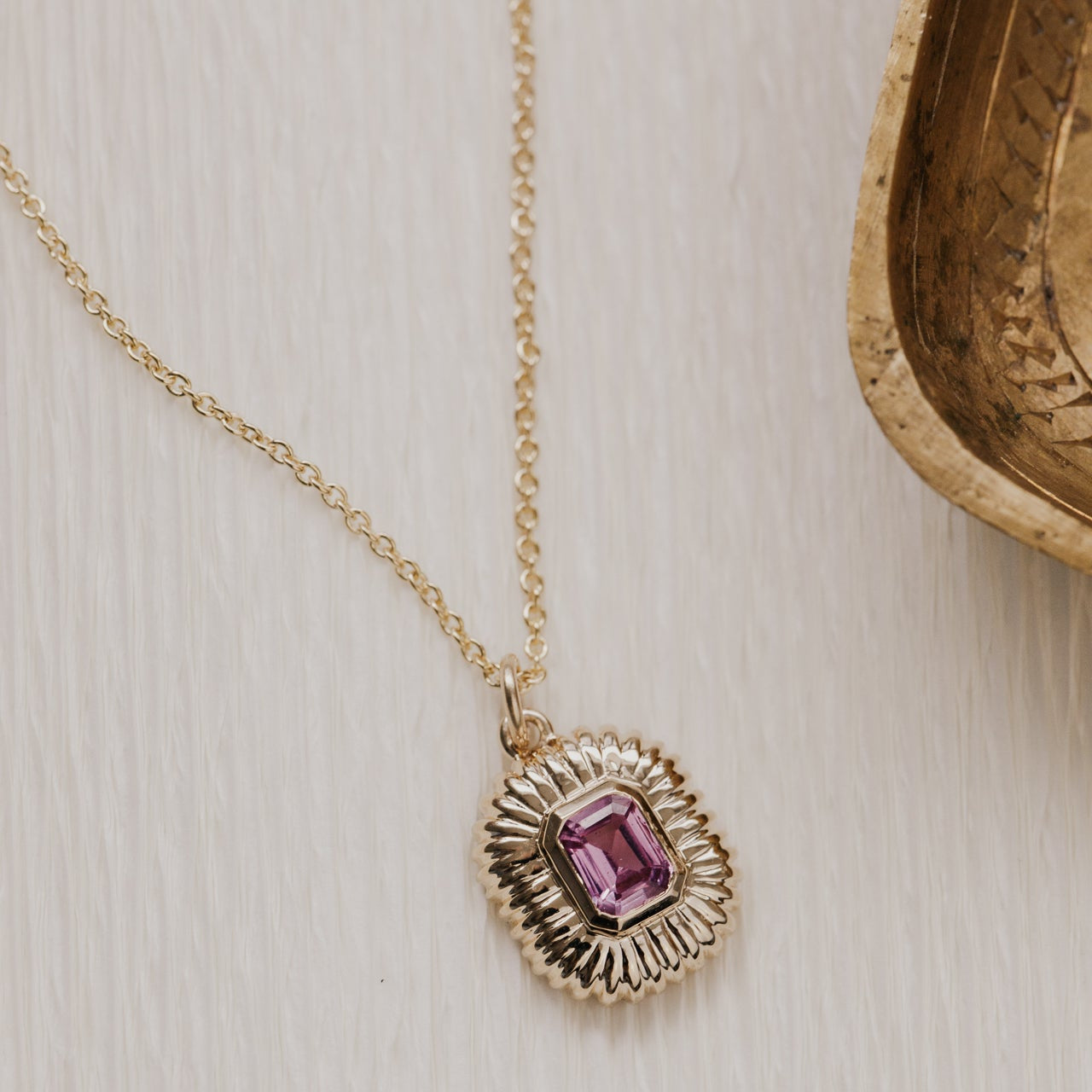 Gold necklace with a pink sapphire gemstone pendant on a light wooden surface