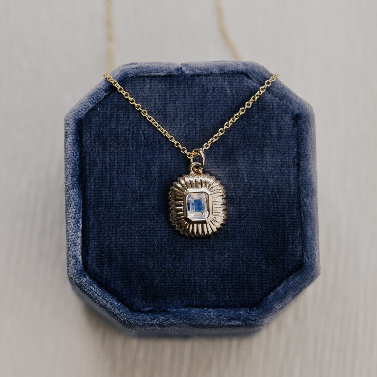 Gold necklace with a moonstone pendant on a blue velvet stand against a light wooden background
