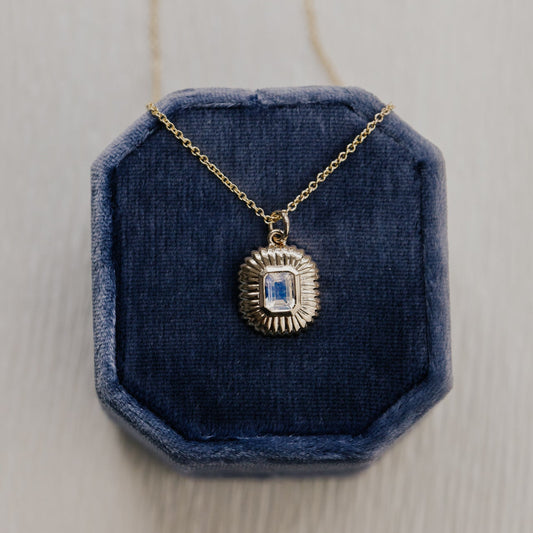Gold necklace with a moonstone pendant on a blue velvet stand against a light wooden background