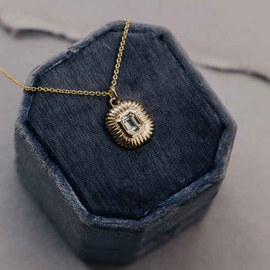 Gold necklace with a green amethyst pendant on a blue cushion