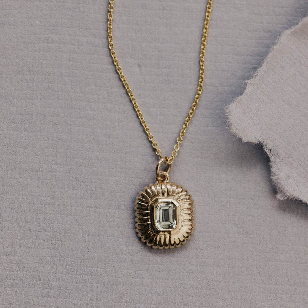 Gold necklace with a green amethyst pendant on a gray textured background