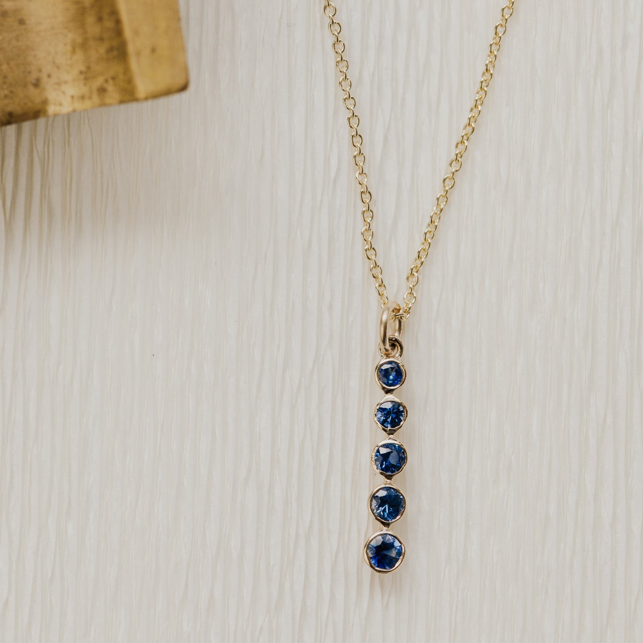 Gold necklace with blue sapphire gemstones on a wooden surface