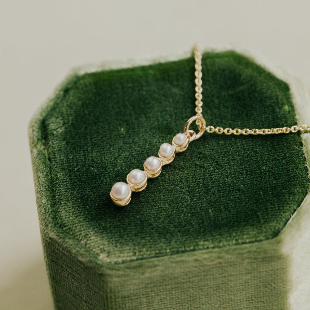 Pearl necklace on a green velvet cushion with a neutral background