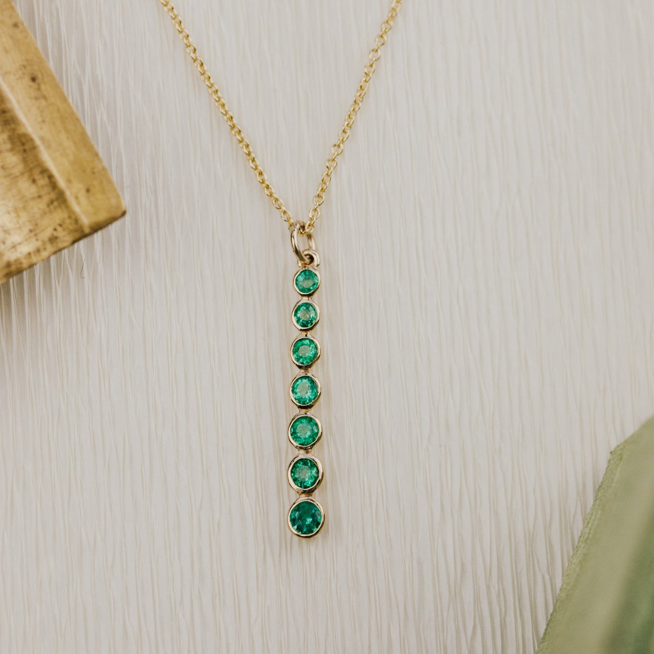 Gold necklace with green emerald gemstones on a textured beige surface