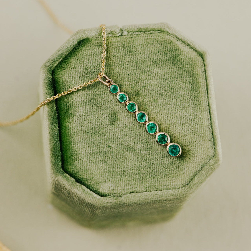 Necklace with green emerald gemstones on a green velvet cushion