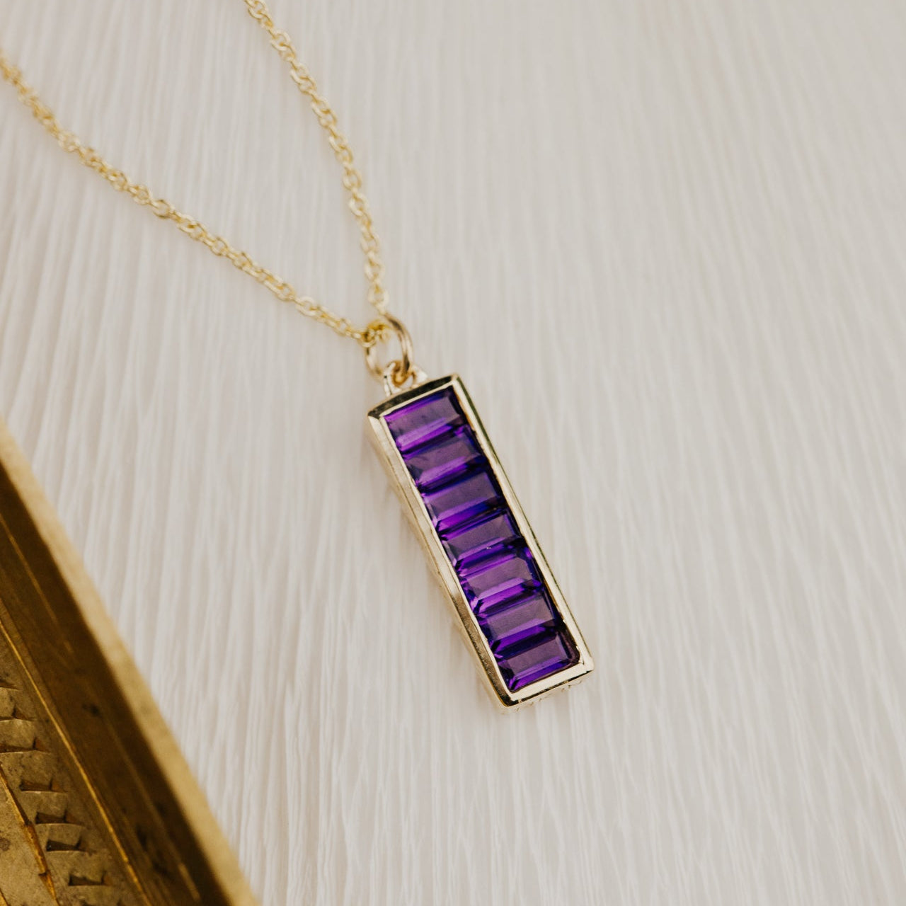 Gold necklace with a purple amethyst pendant on a textured surface