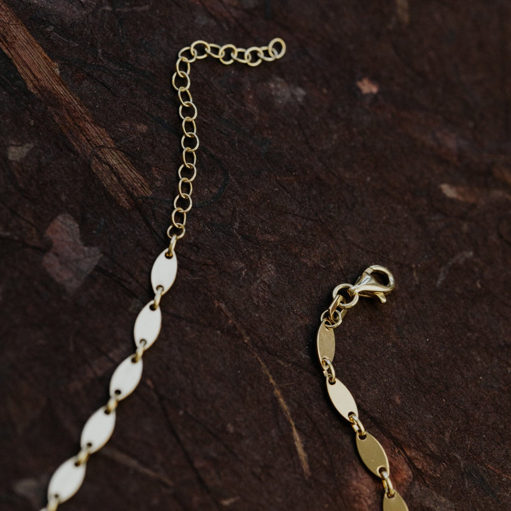 Gold chain necklace with a clasp on a dark brown surface