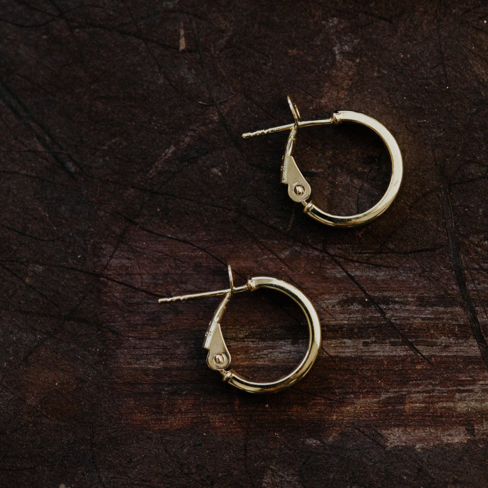 Gold hoop earrings on a dark wooden surface