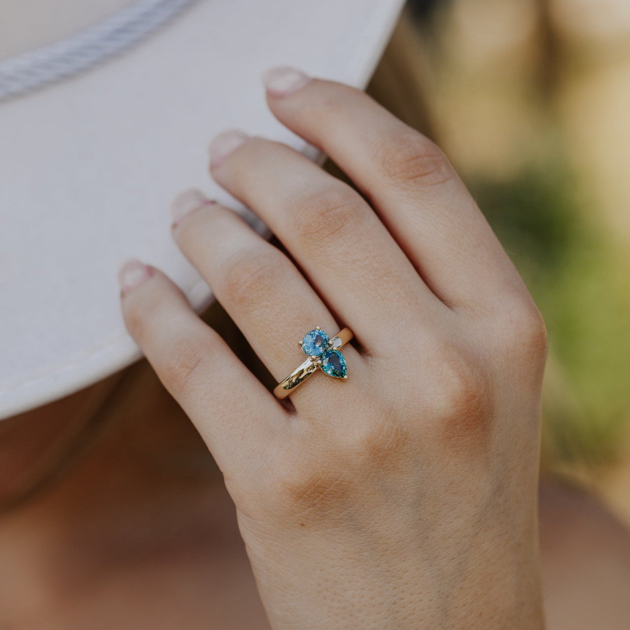 Hand wearing a gold ring with blue Montana sapphire gemstones against a blurred background