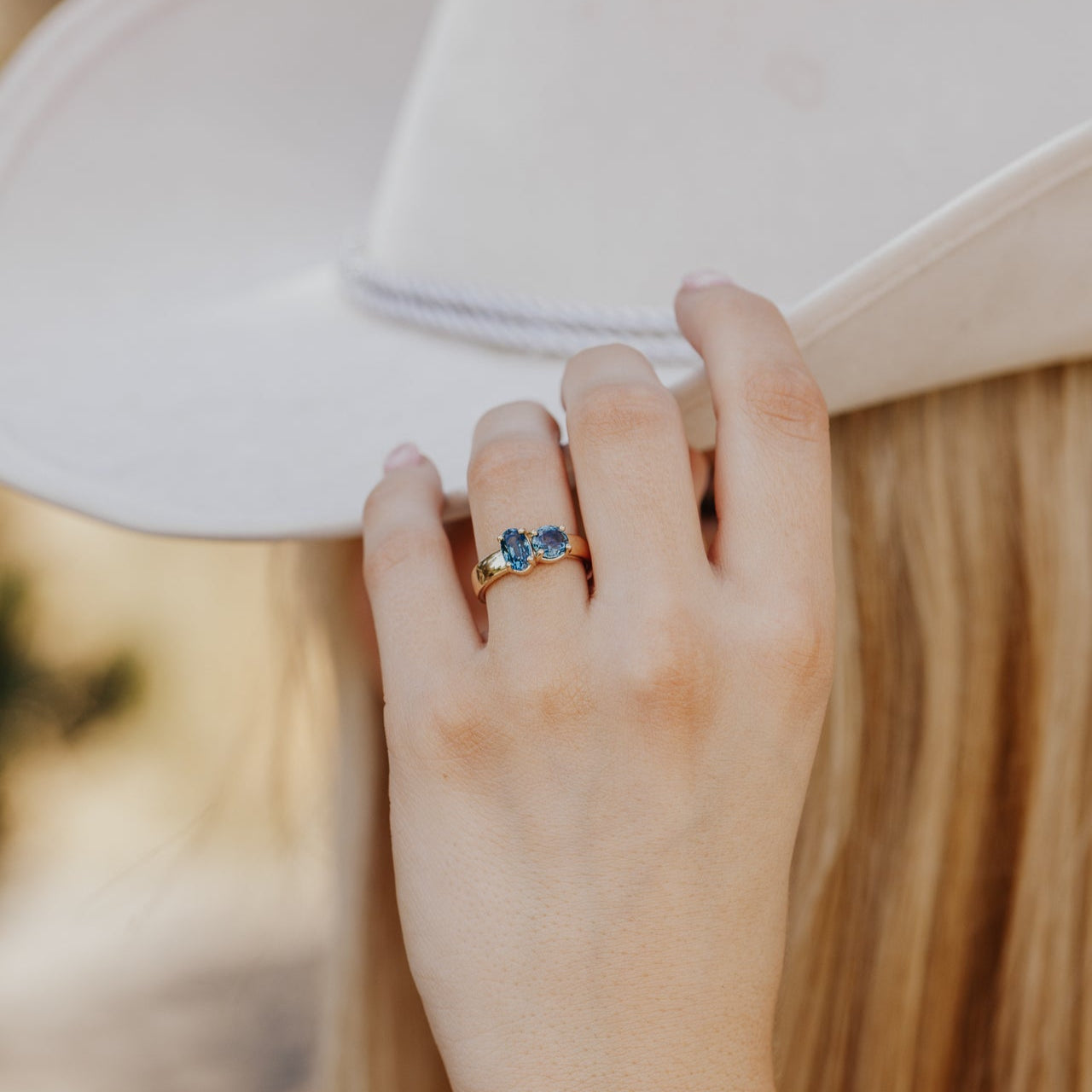 Hand wearing a ring with blue Montana sapphire gemstones against a blurred background