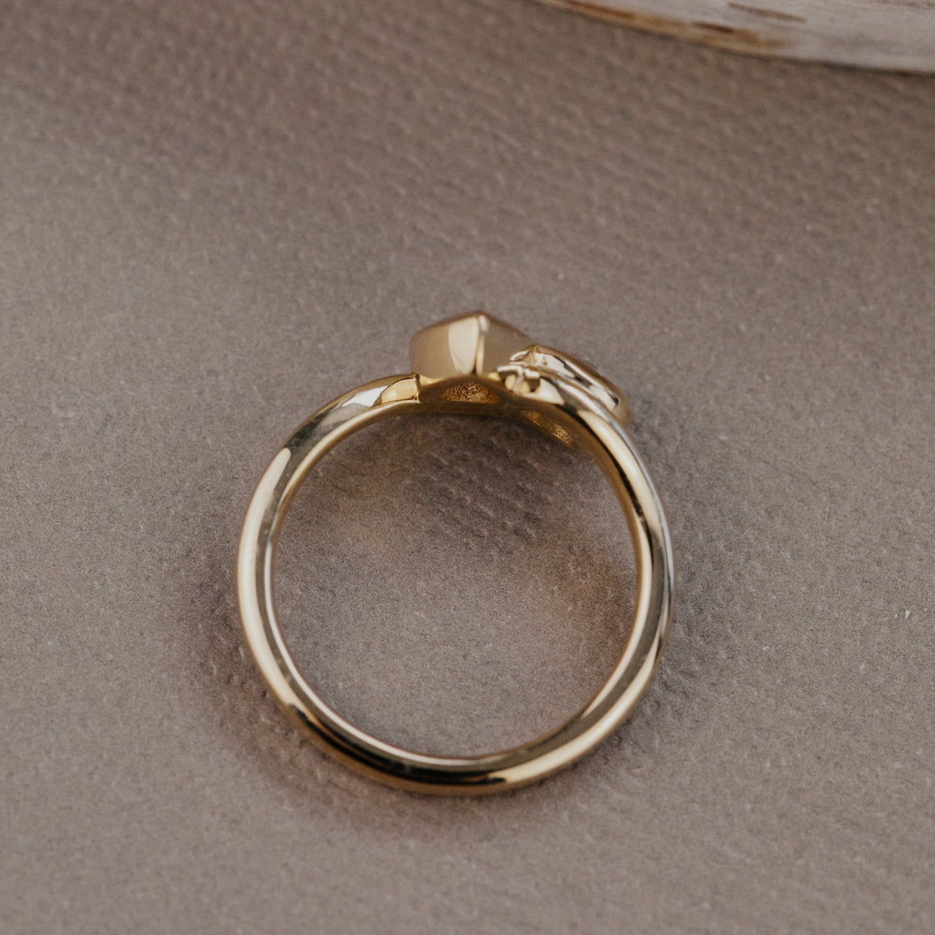 Gold ring on a textured beige surface with a wooden object in the background.