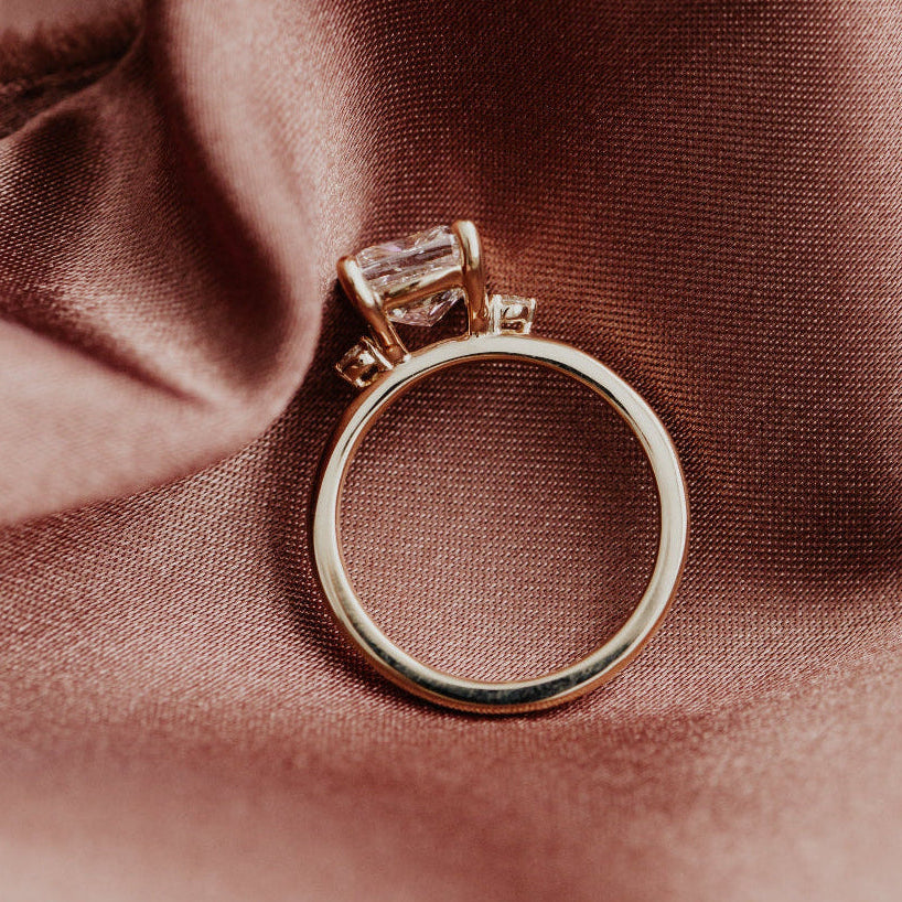 Gold engagement ring with a diamond on a brown fabric background.