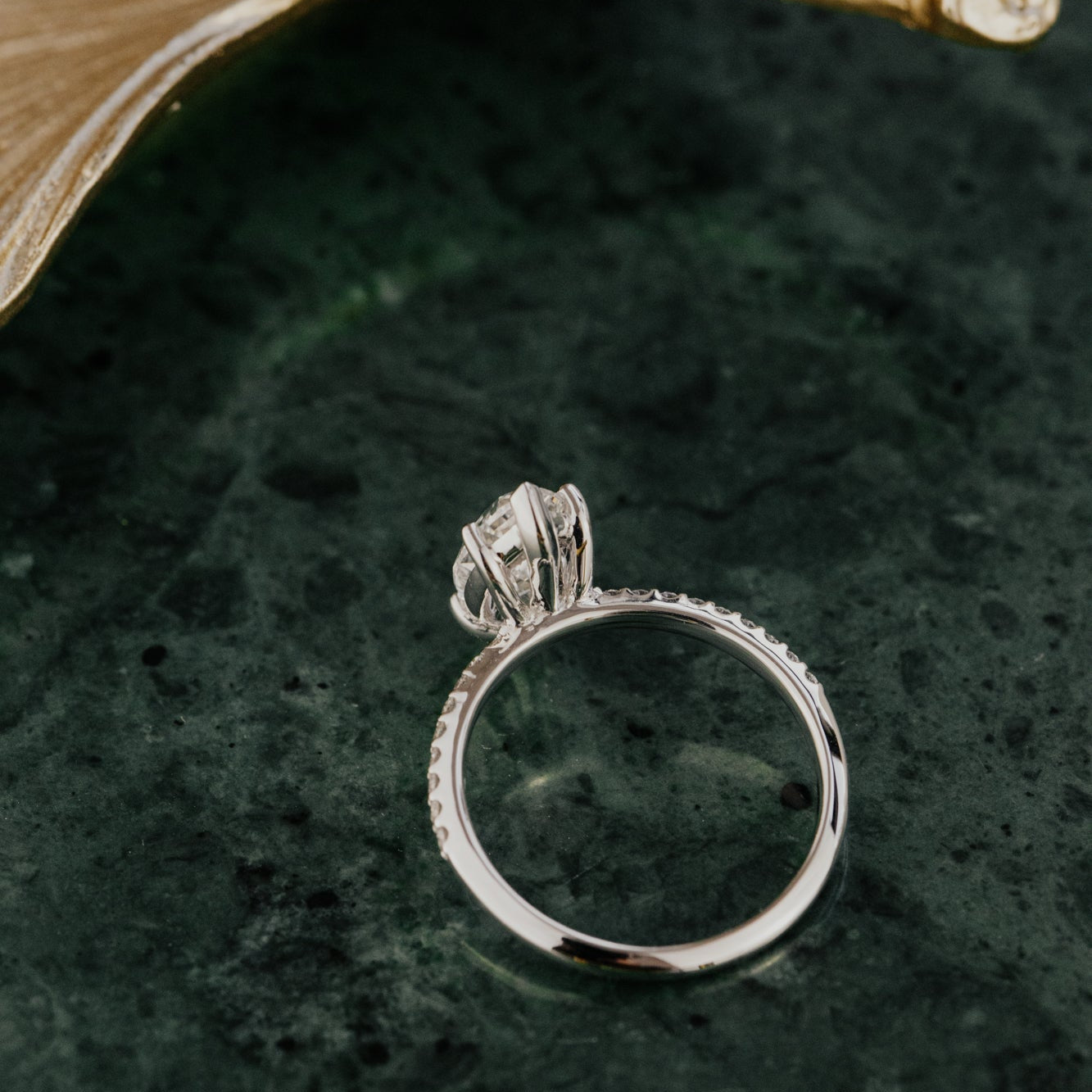 White gold ring with a marquise lab grown diamond on a dark green surface.