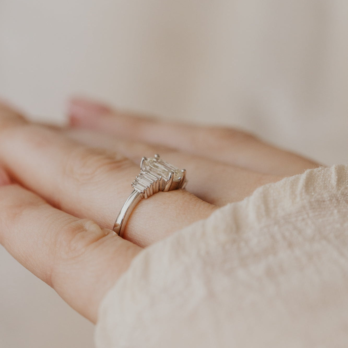 White gold ring with a elongated cushion diamond on a hand against a neutral background.