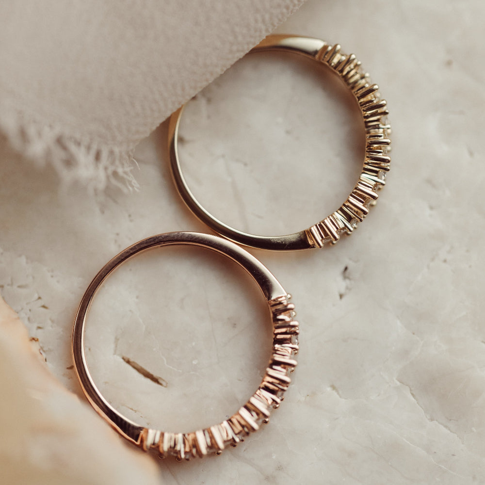 Rose and yellow gold diamond wedding bands on a textured beige surface.