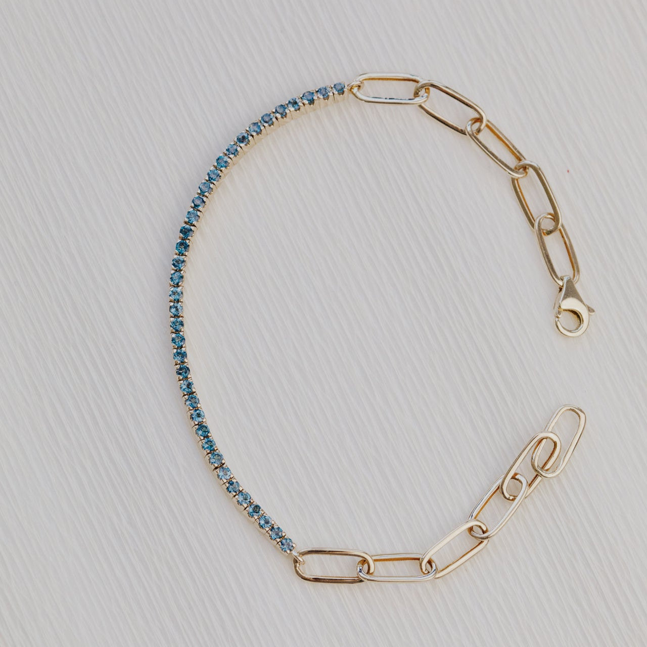 Gold chain bracelet with blue topaz on a light gray background