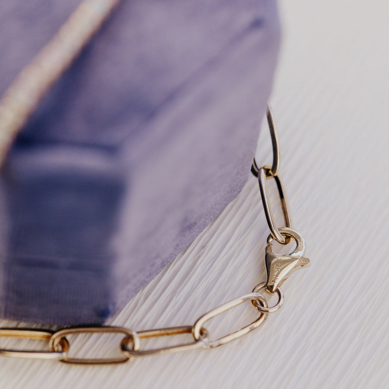 Gold chain bracelet on a light wooden surface with a blurred purple object in the background