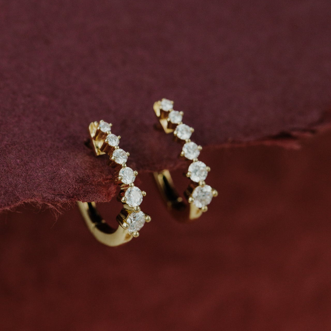 Gold hoop earrings with diamond accents on a burgundy fabric background