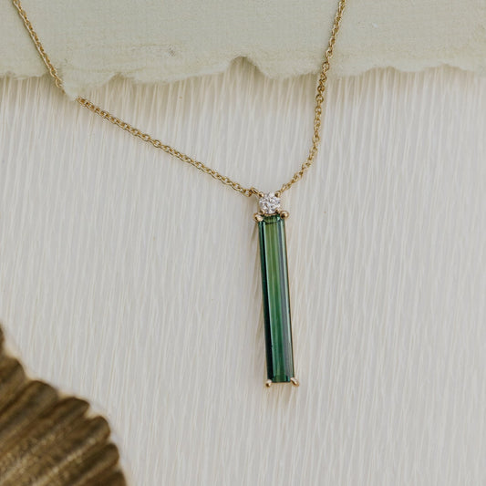 Gold necklace with a green tourmaline pendant on a textured white surface