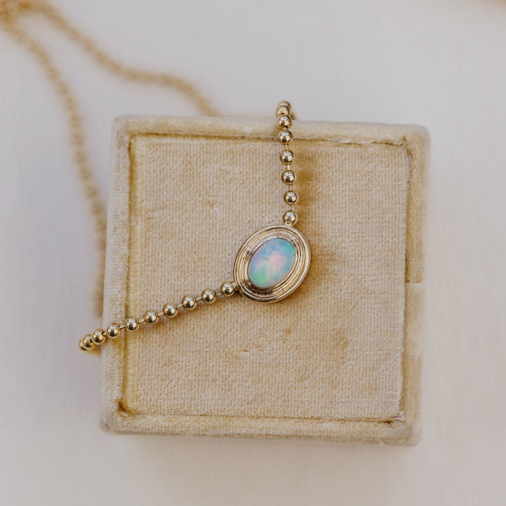 Gold necklace with an opal pendant on a beige jewelry display box.