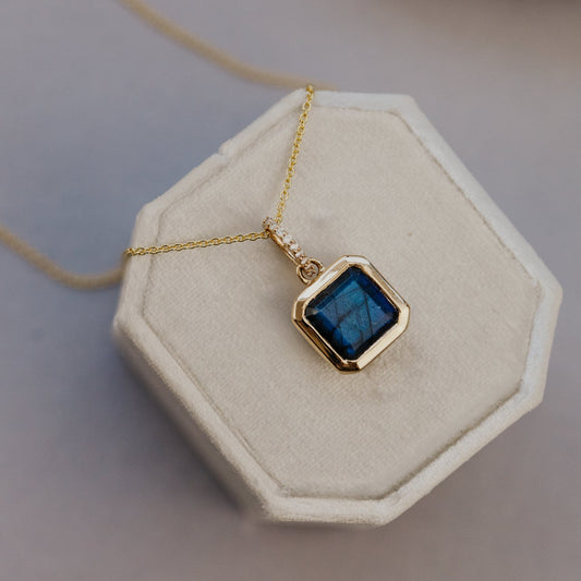 Necklace with a blue labradorite pendant on a beige hexagonal stand
