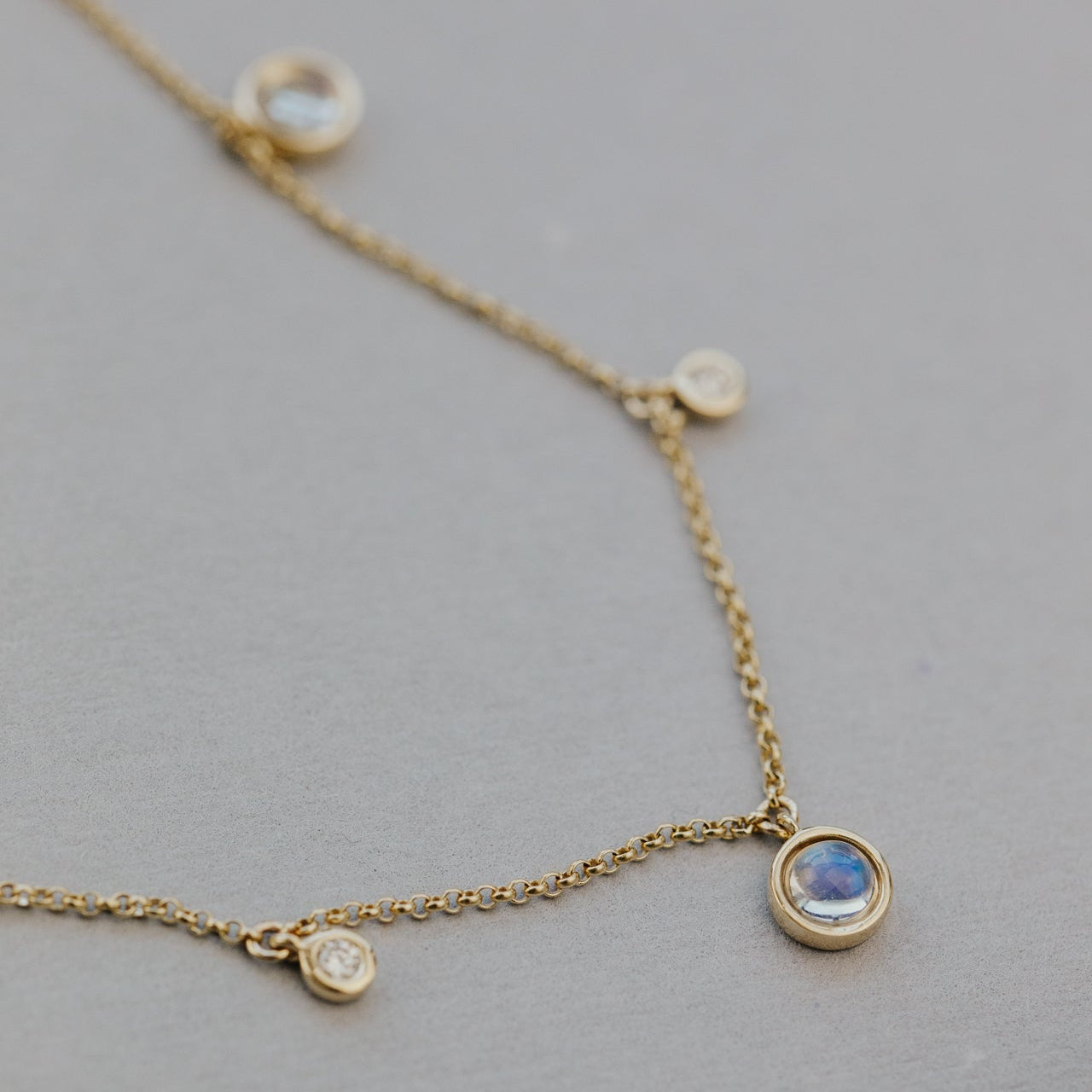 Gold necklace with moonstone and diamond pendants on a gray background