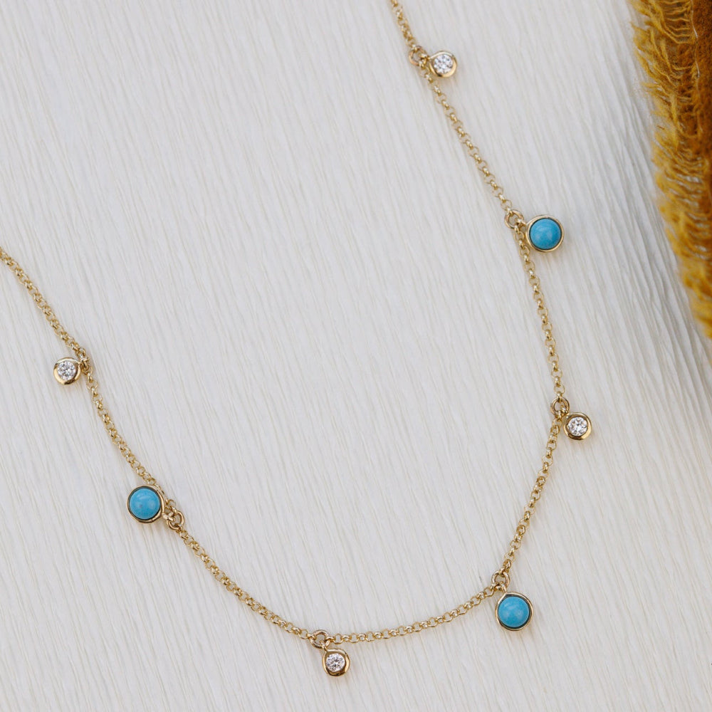 Gold necklace with turquoise and diamond stones on a white fabric background
