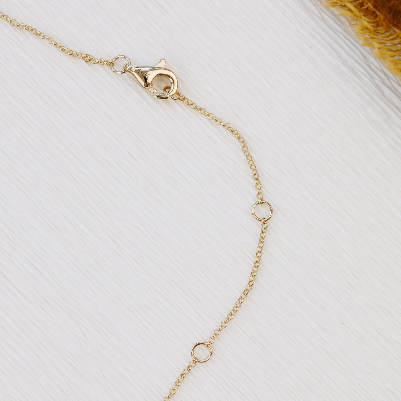 Gold necklace on a white surface with a brown textured object in the corner