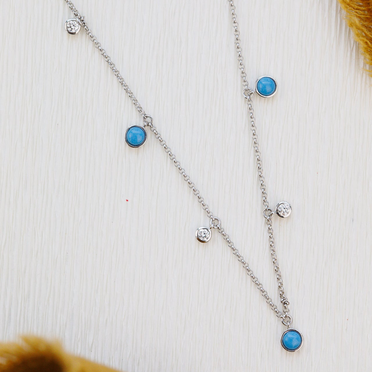 white gold necklace with turquoise and diamond gemstones on a textured white surface