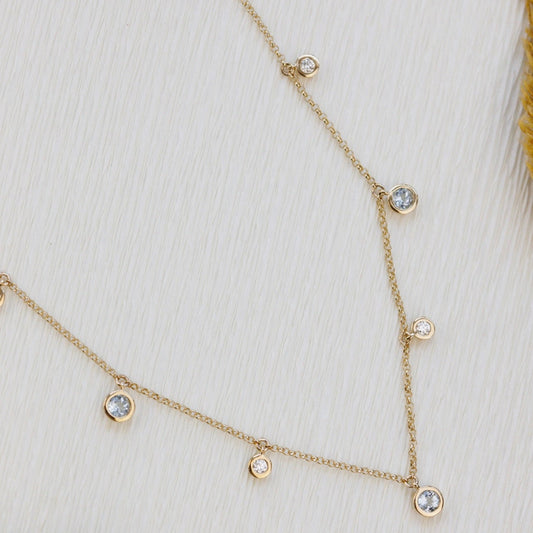 Delicate gold necklace with aquamarine and diamond gemstones on a white background
