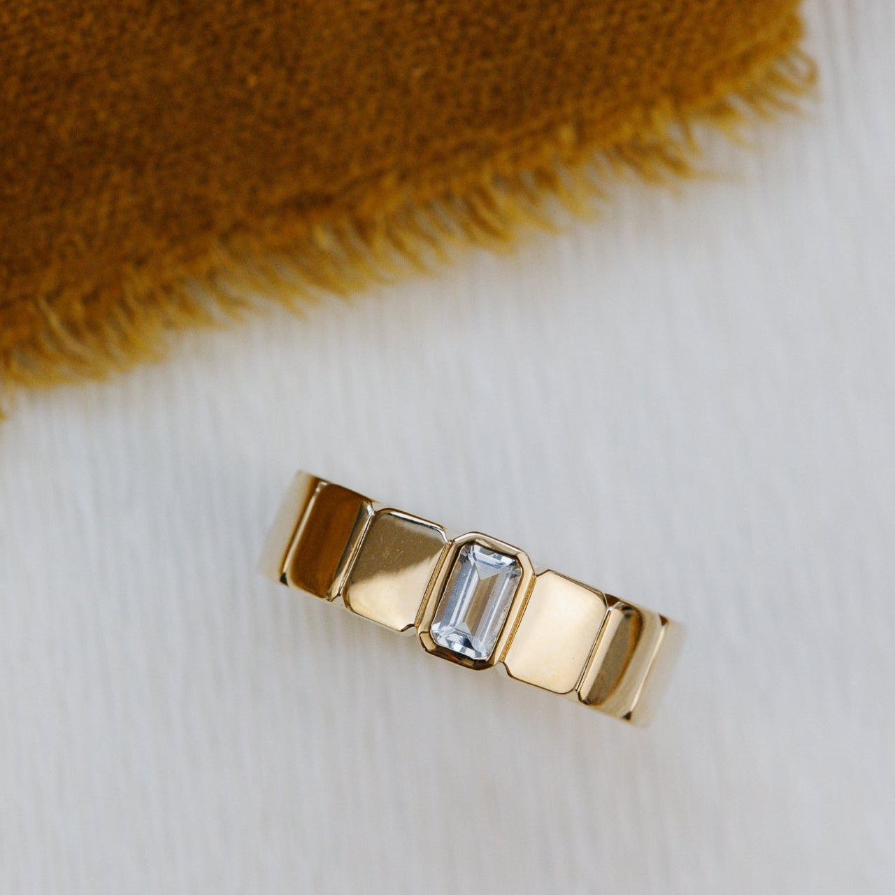 Gold ring with a central gemstone on a textured fabric background
