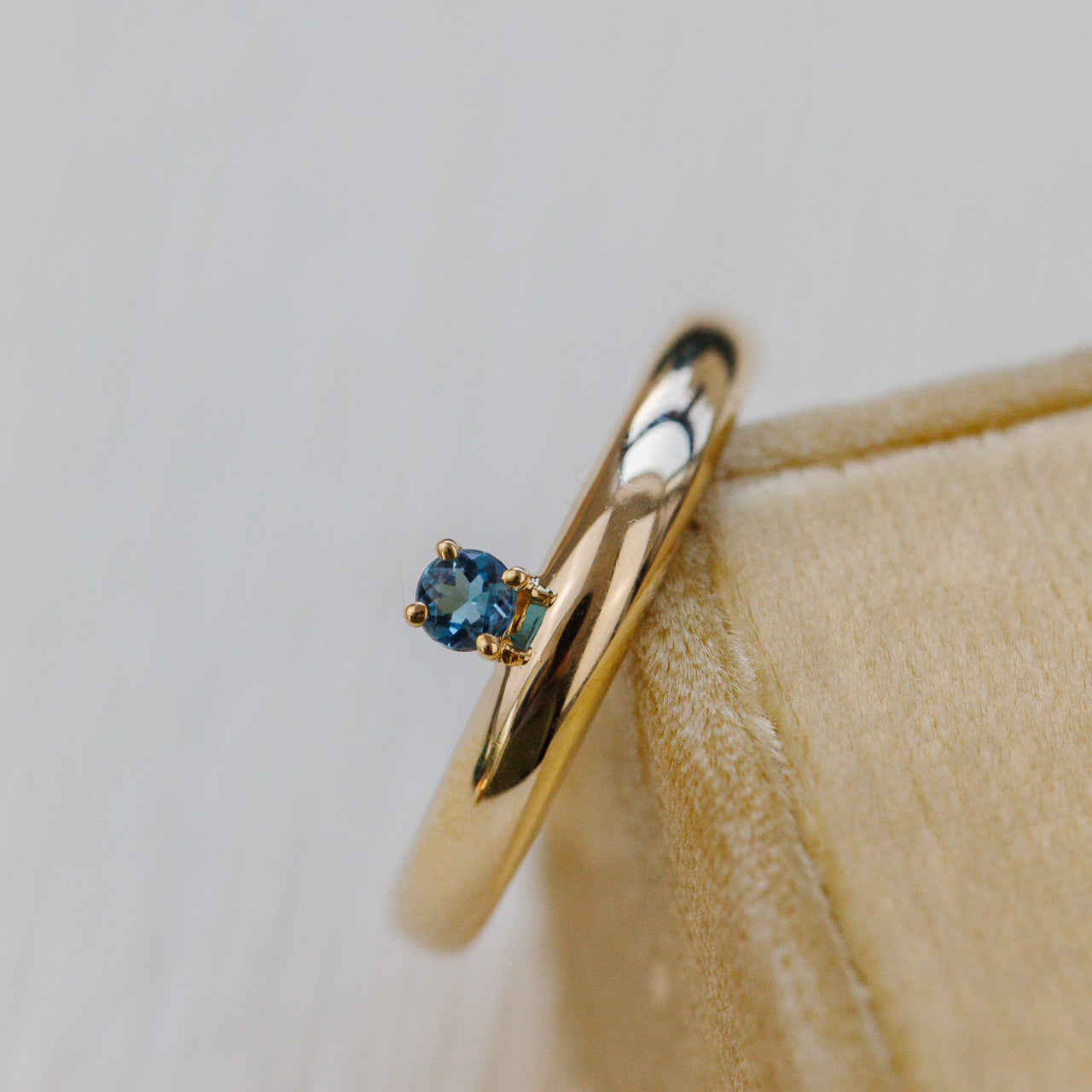 Gold ring with a blue gemstone on a beige surface