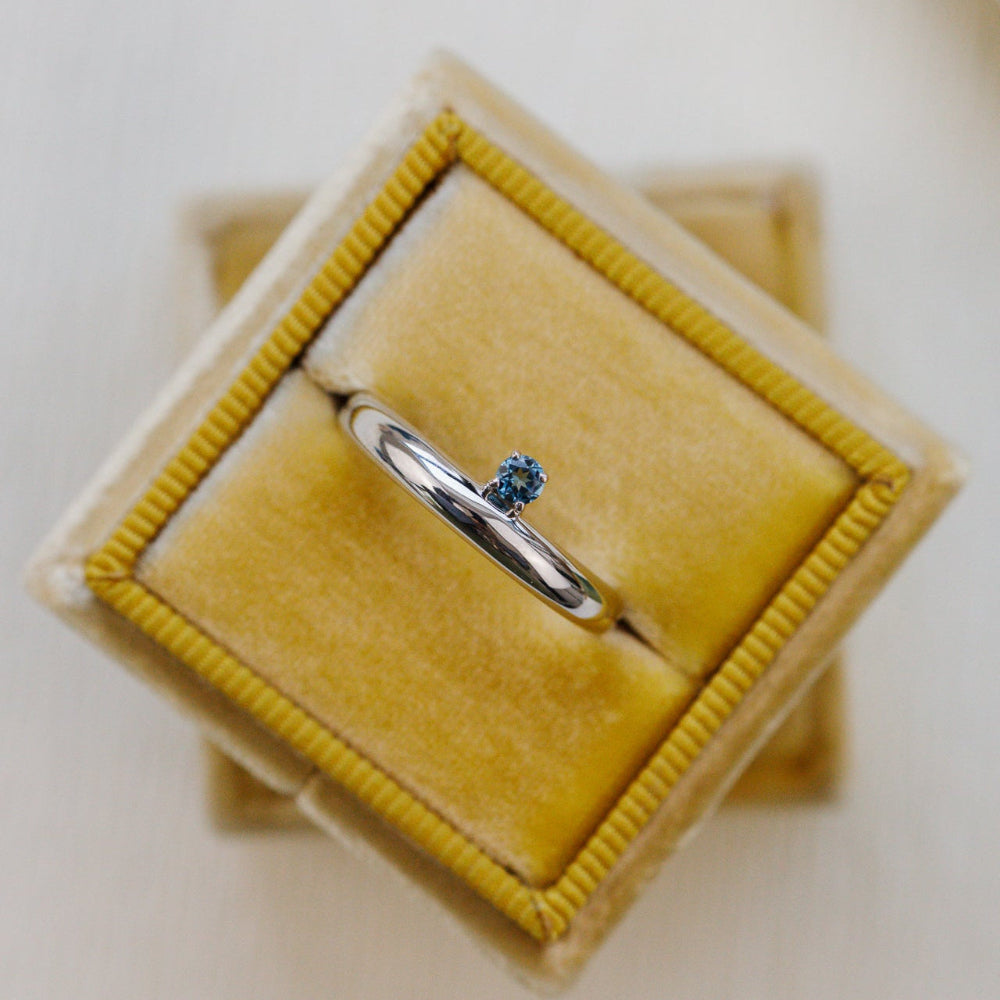 Silver ring with a blue stone in a yellow velvet box on a light background