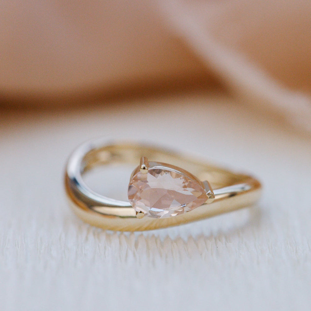 Gold ring with pear-shaped gemstone on a soft beige background