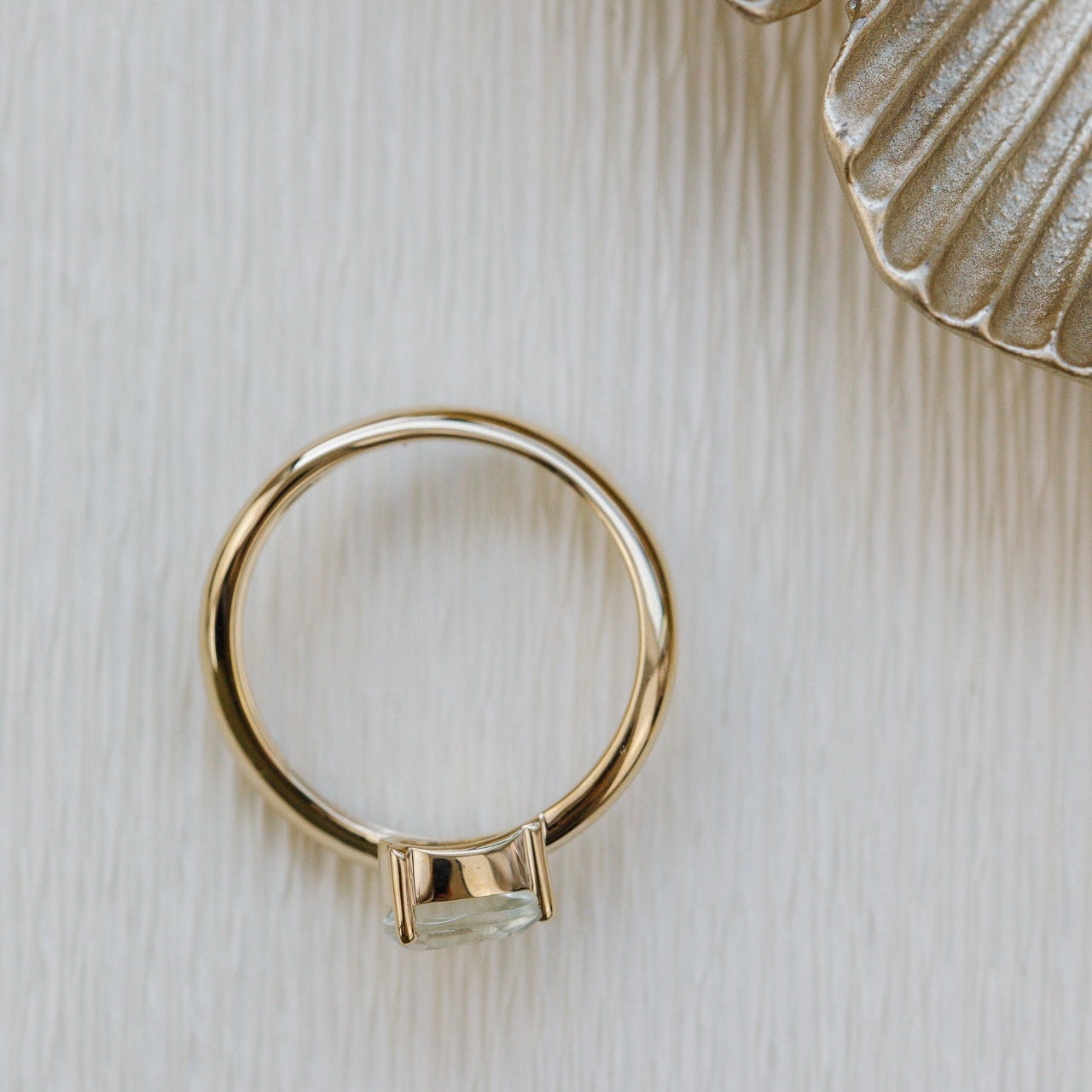 Gold ring with a green gemstone on a textured beige surface