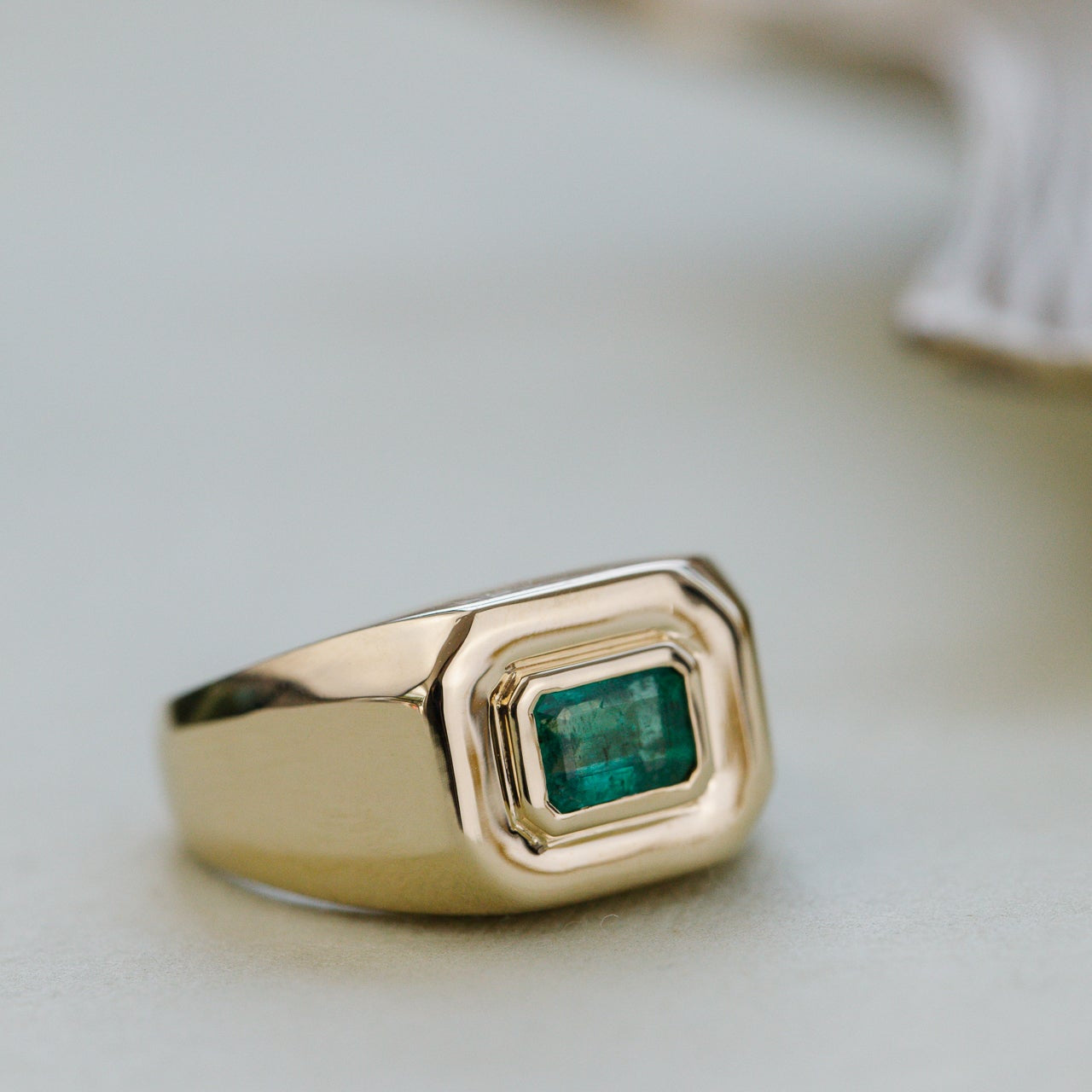 Gold ring with a green emerald gemstone on a light background