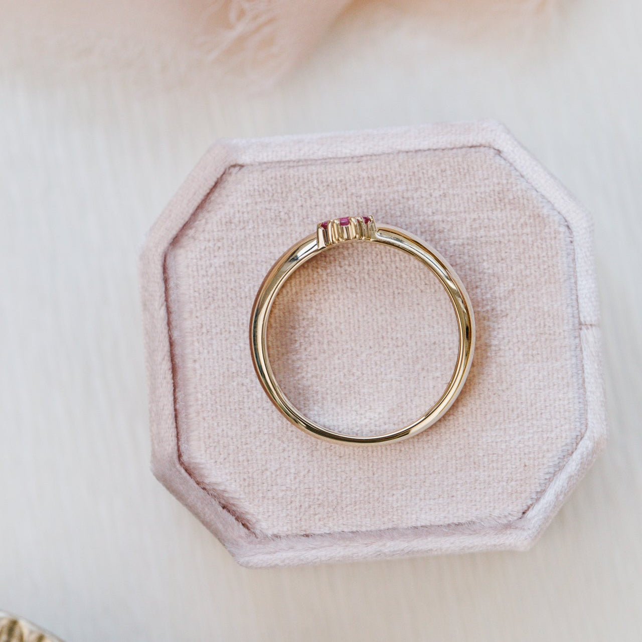 Gold ring on a hexagonal pink fabric cushion with a soft pink background