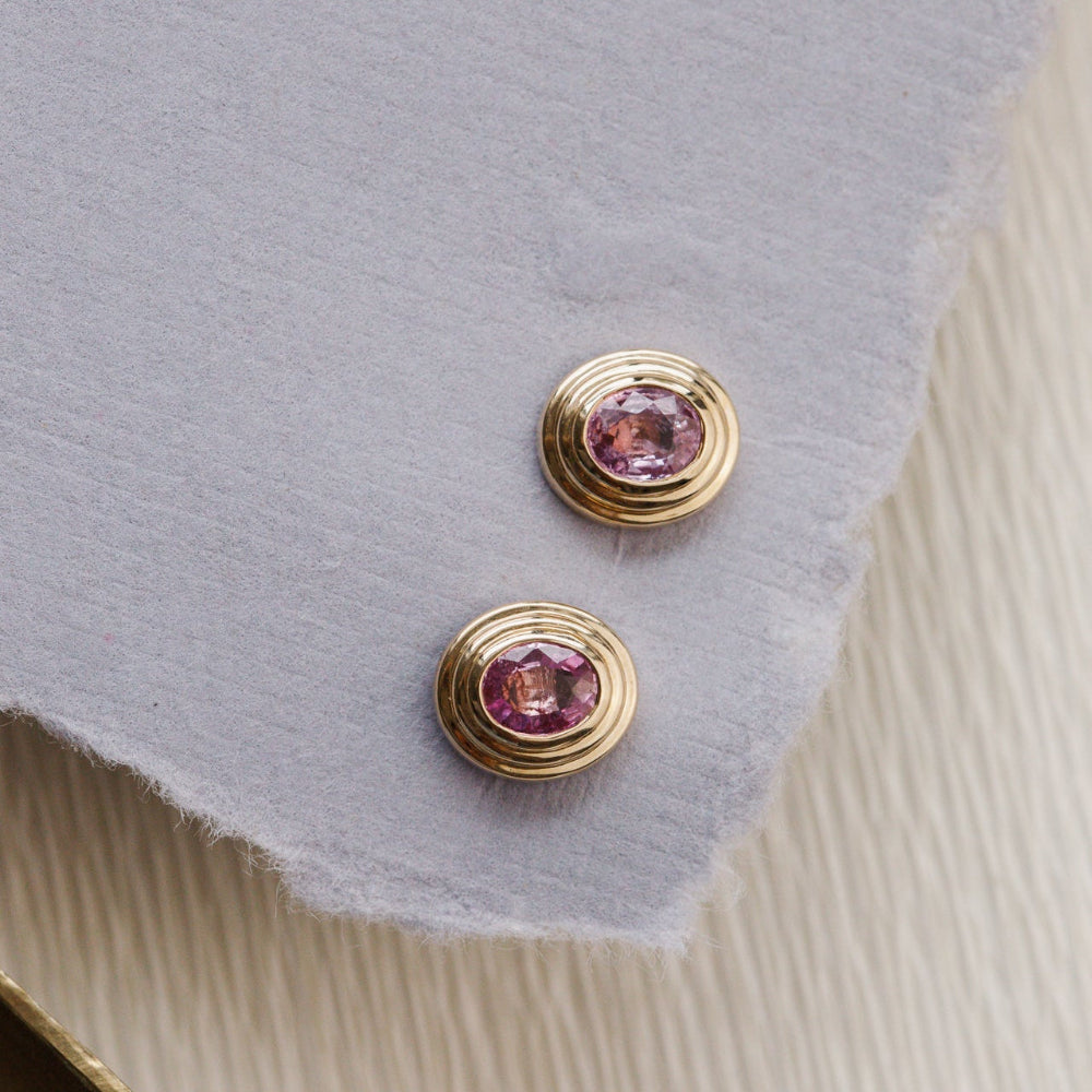 Gold earrings with pink sapphires gemstones on a textured surface