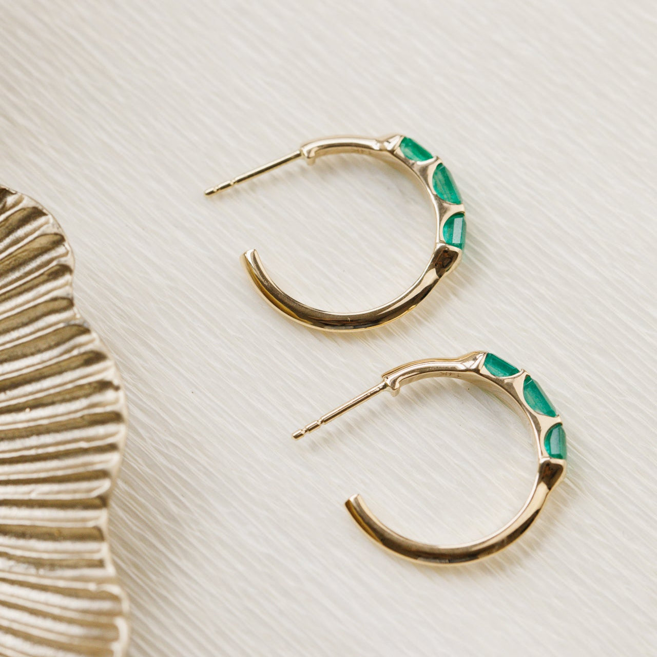 Gold hoop earrings with green accents on a textured beige surface