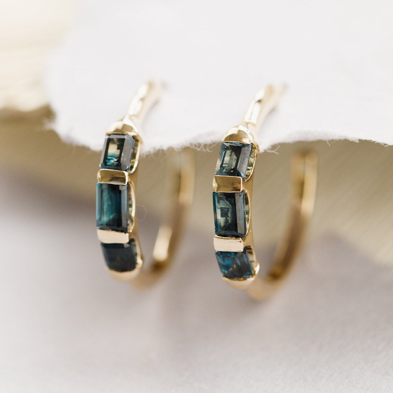 Gold hoop earrings with blue topaz gemstones on a white background