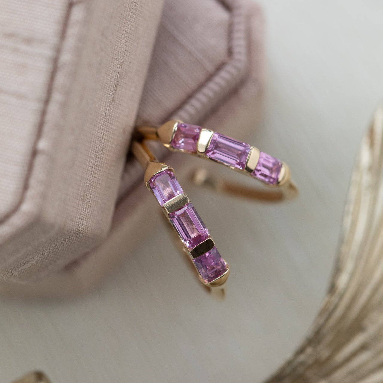 Gold hoop earrings with pink sapphire gemstones on a neutral background