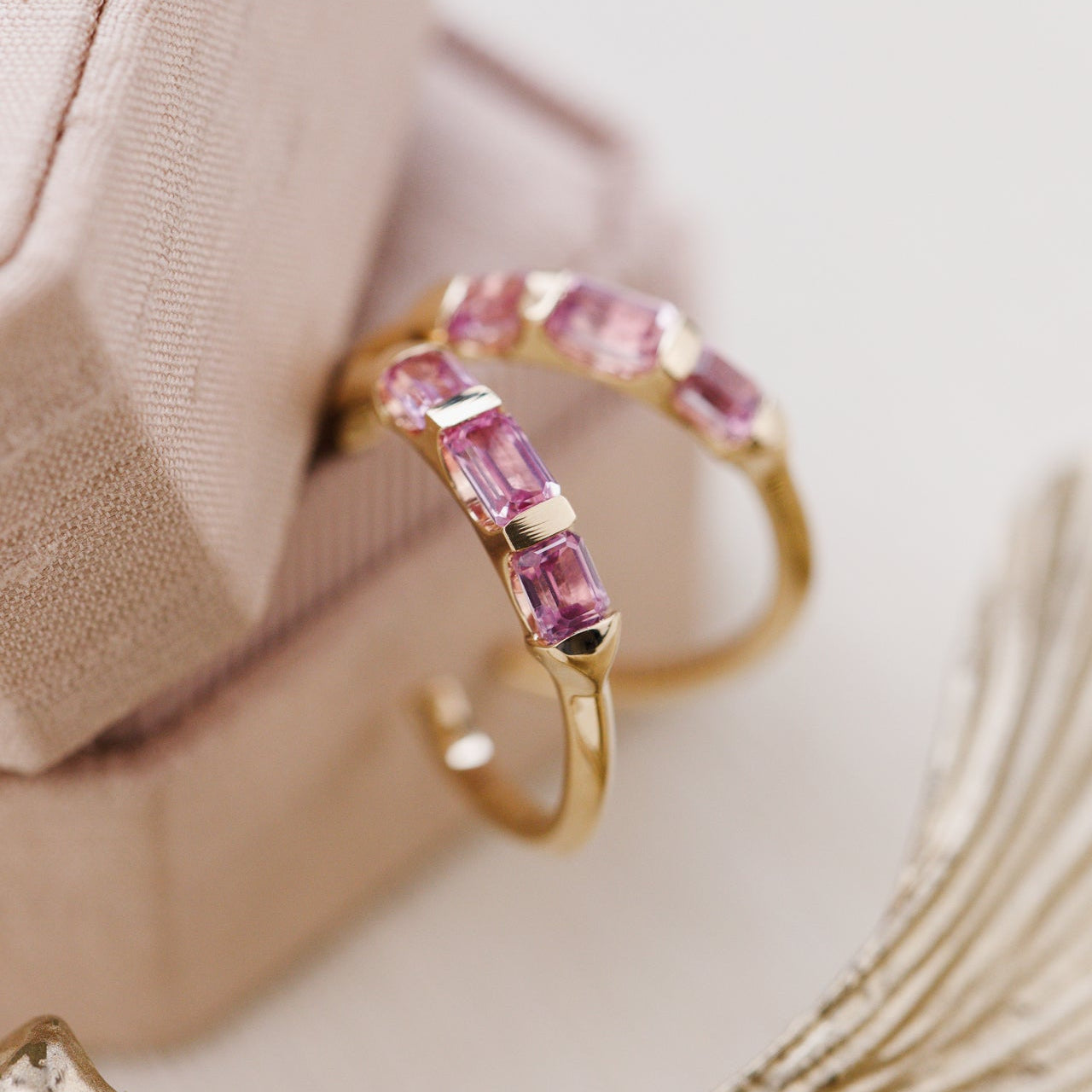 Gold earring with pink sapphire gemstones on a neutral background