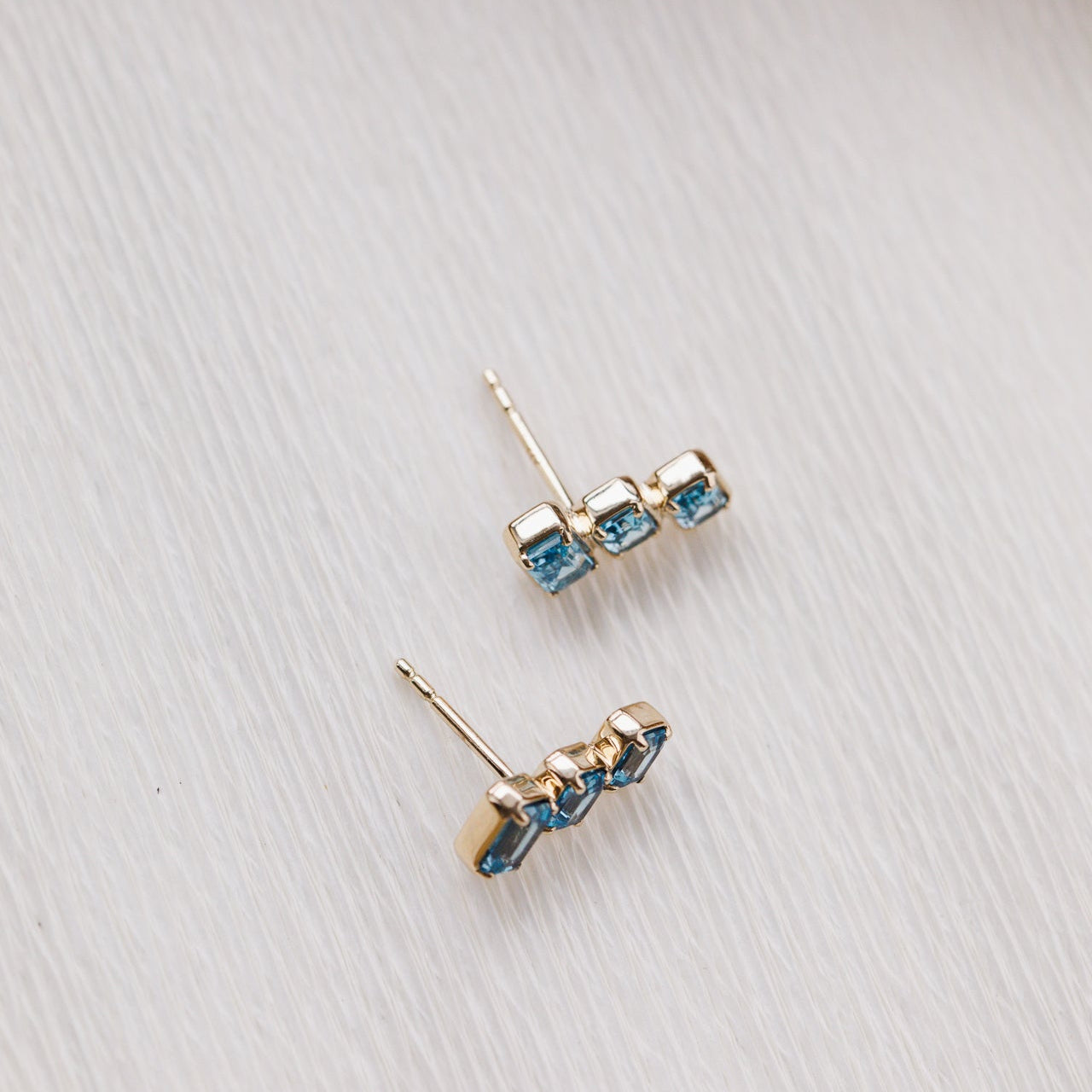 Pair of gold earrings with blue gemstones on a light gray surface