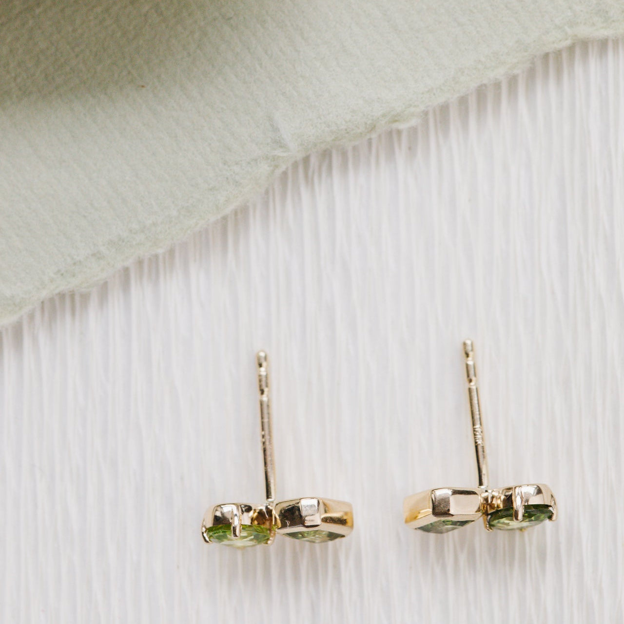 Gold earrings with green gemstones on a textured white background