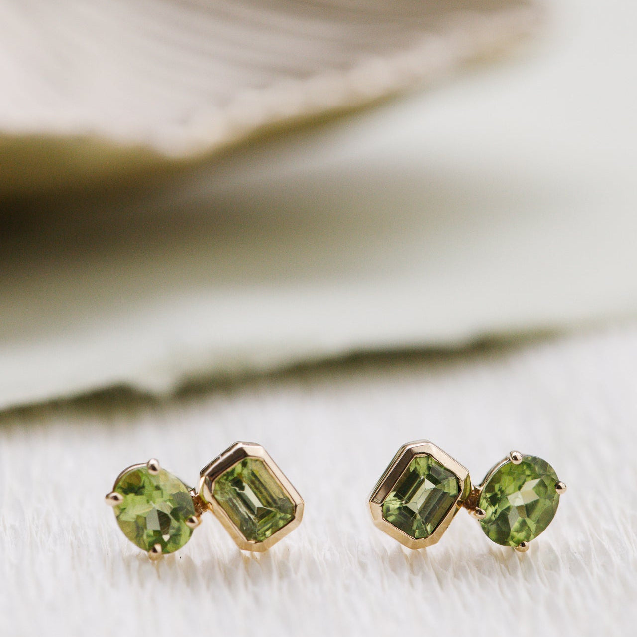 Green gemstone stud earrings on a white surface with a blurred background